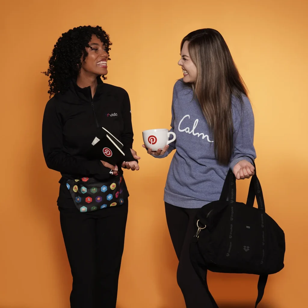 Women holding branded mugs and bags, smiling