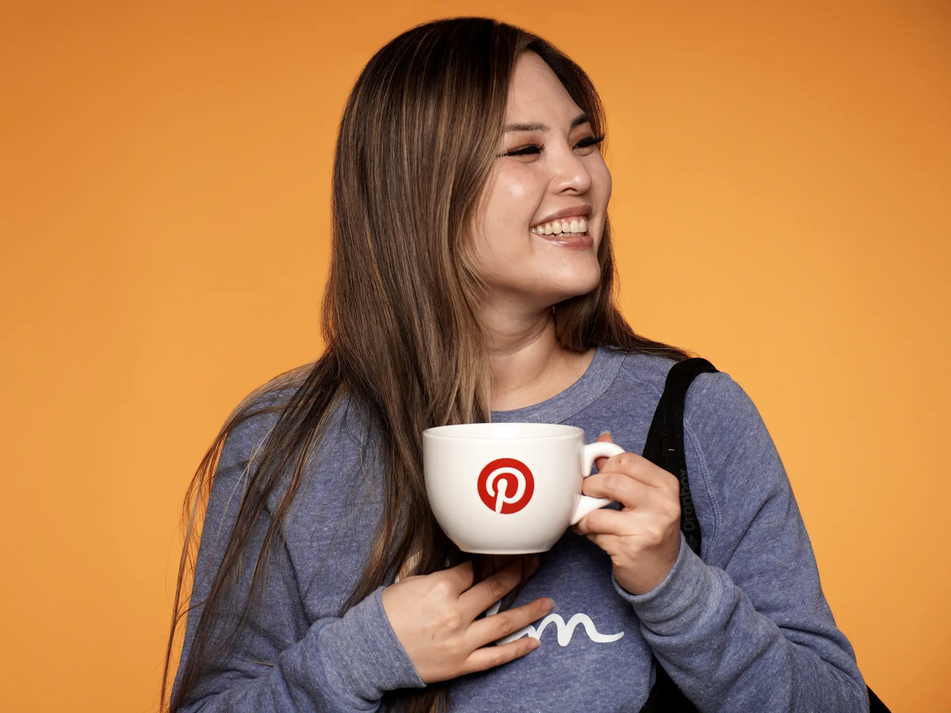 Smiling woman holding Pinterest mug on orange background