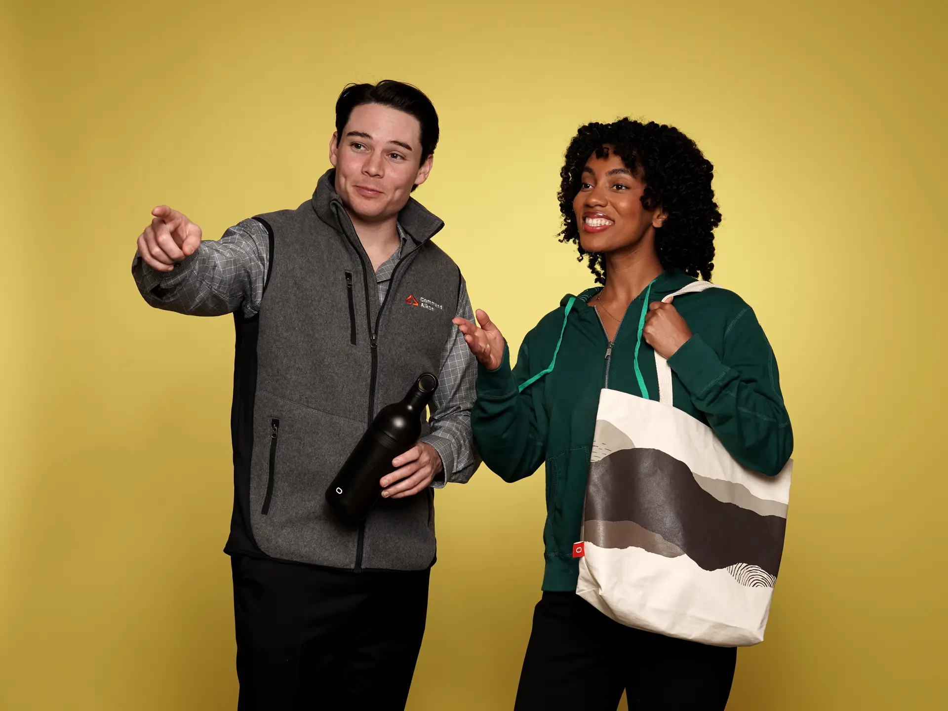 Duo with branded water bottle and tote bag on yellow background