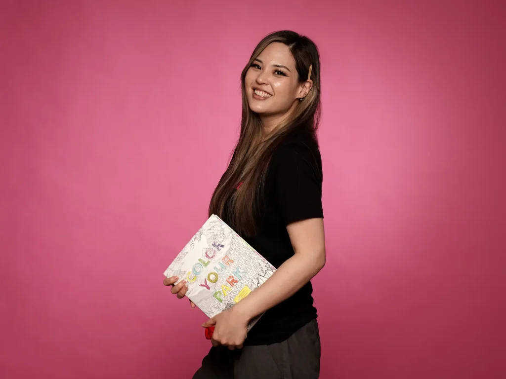 Smiling woman with coloring book on pink background