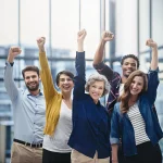 Diverse group of happy professionals celebrating teamwork and success in modern office, symbolizing employee recognition and corporate gifting solutions.