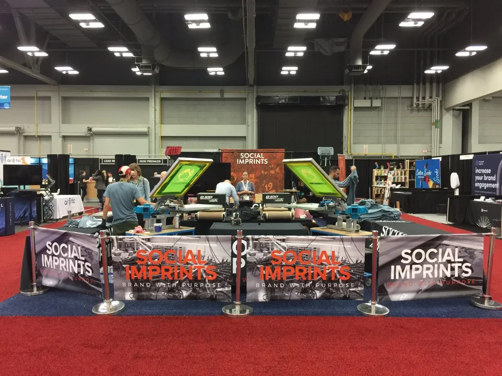 Live screen printing booth by Social Imprints at trade show, showcasing custom branded merchandise and promotional products for corporate swag and event giveaways.