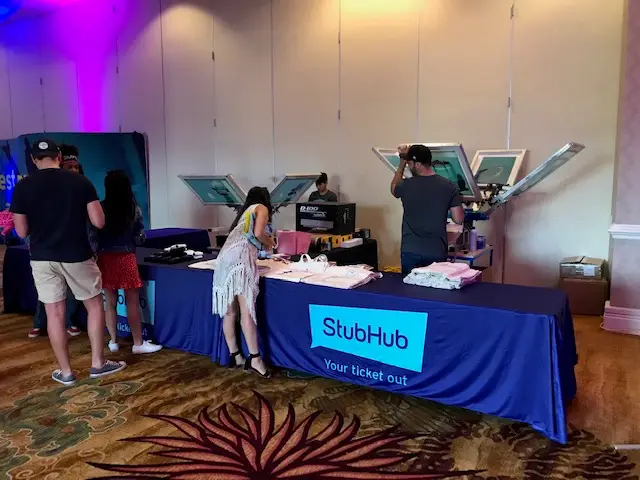 Live screen printing station at corporate event featuring custom branded apparel and promotional products, showcasing expert swag company services for giveaways and employee gifts.