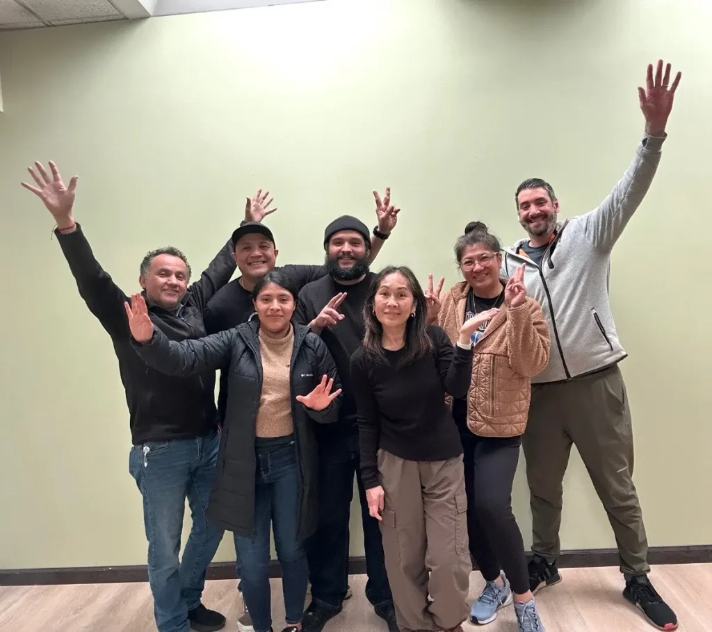 Diverse team of smiling professionals posing with raised hands, representing a customer-focused corporate swag company committed to quality and social responsibility.