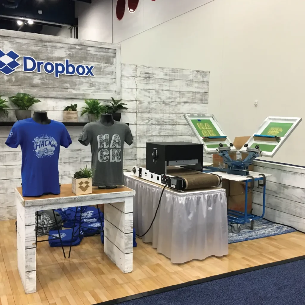 Screen-printing setup with custom branded Dropbox event t-shirts on mannequins, showcasing live printing and promotional swag for corporate events and trade shows.