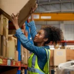 Warehouse worker organizing branded promotional product boxes in fulfillment center for corporate swag and event giveaways.