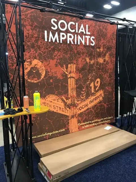 Social Imprints branded trade show booth backdrop featuring custom promotional products and sustainable swag solutions for corporate events and employee gifting.
