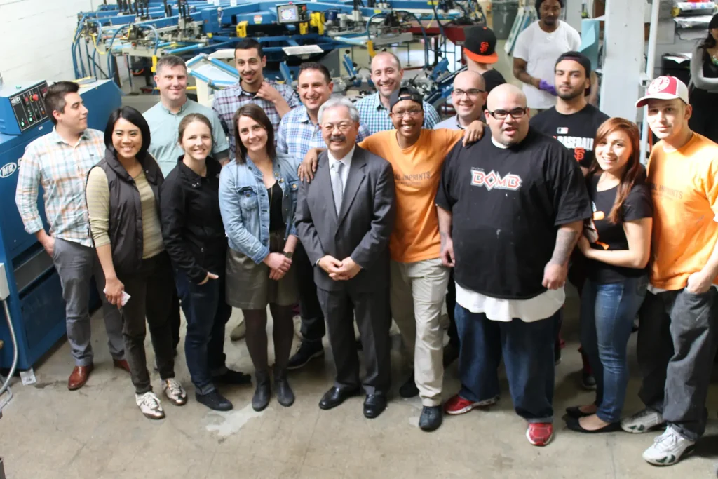 Diverse Social Imprints team posing in San Francisco print shop, experts in custom branded merchandise, live screen printing, corporate swag, and sustainable promotional products.