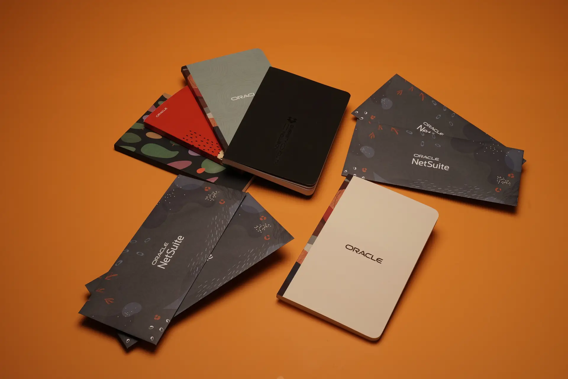 Custom branded Oracle NetSuite notebooks and envelopes on orange background, showcasing premium promotional products for corporate events and employee gifts by top swag company.
