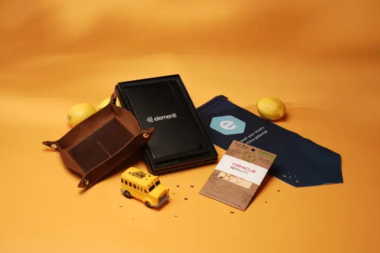 Custom branded corporate swag items including a leather valet tray, branded tech gadget box, promotional seed packet, and company logo bandana, showcased on an orange background for sustainable event giveaways and employee gifts.