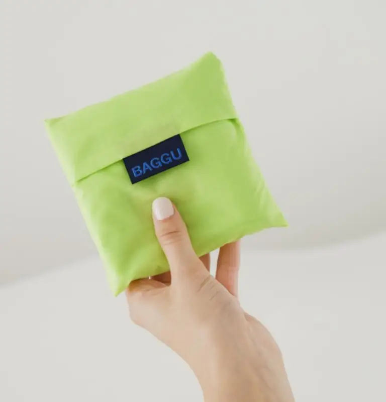 Hand holding a compact, reusable green BAGGU pouch, ideal eco-friendly promotional product and sustainable swag giveaway for corporate events and employee gifts.