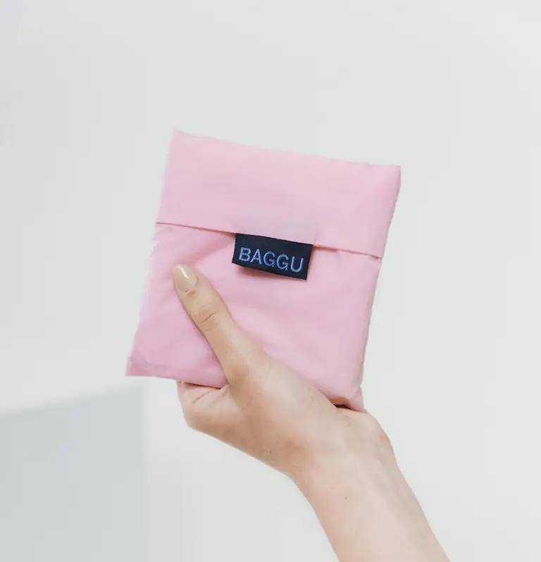 Hand holding a folded pink BAGGU reusable eco-friendly tote bag, ideal for sustainable promotional swag and corporate giveaway items.