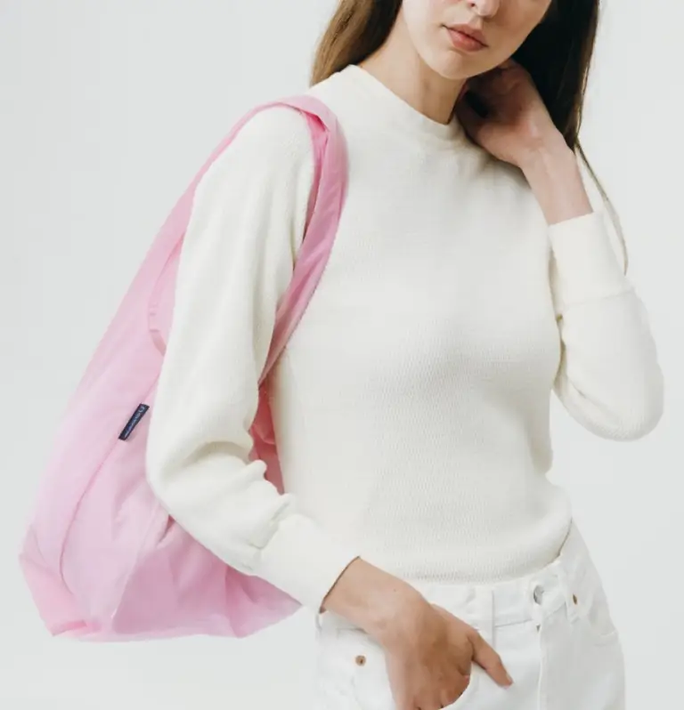 Woman wearing white sweater and jeans carrying a pink reusable tote bag, eco-friendly promotional swag item for corporate events and giveaways.
