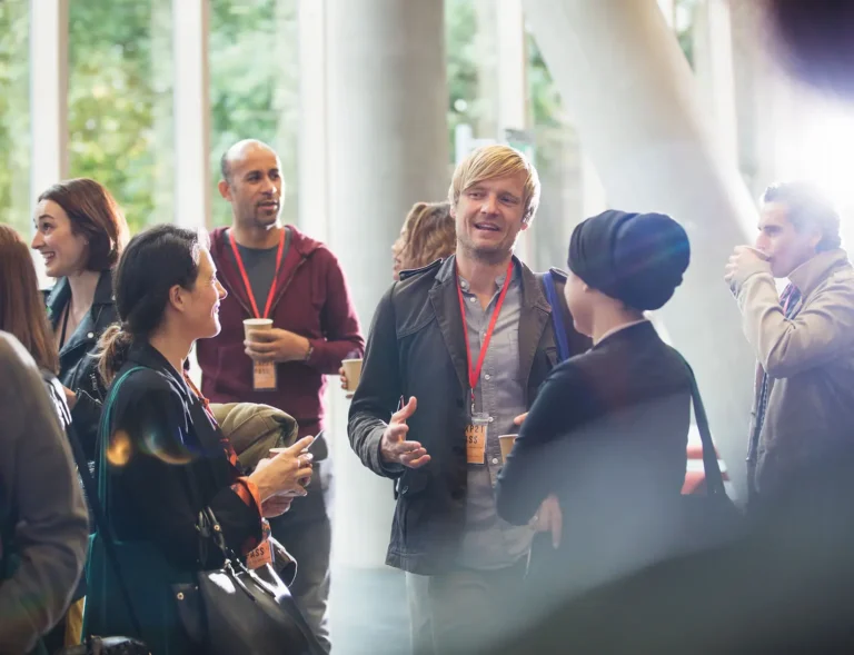 Networking professionals wearing event badges and enjoying coffee during a corporate conference break, ideal for showcasing swag items for events and corporate gifting solutions.