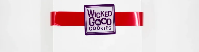 White promotional box with red ribbon and custom branded "Wicked Good Cookies" label, showcasing premium corporate gifting and custom packaging services.