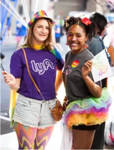 Two smiling women wearing custom branded Lyft apparel and colorful rainbow-themed swag items at a vibrant event, showcasing inclusive corporate swag and promotional products for events.