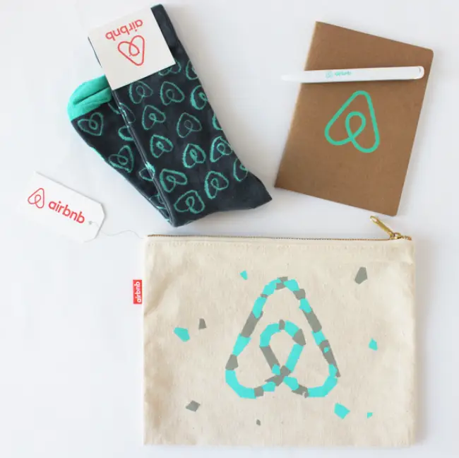 Branded Airbnb promotional swag set including custom printed socks, eco-friendly notebook, pen, and canvas pouch, ideal corporate gifts for events and employee recognition.