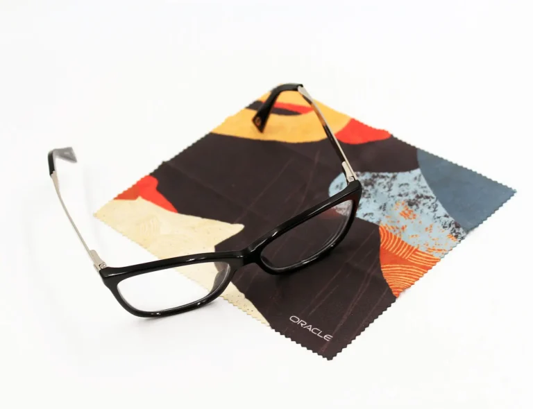 Black rectangular eyeglasses resting on a custom branded colorful microfiber cleaning cloth with Oracle logo, showcasing personalized corporate promotional products and branded swag items for events.