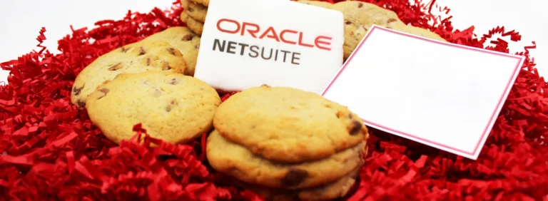 Custom branded Oracle NetSuite promotional cookies with logo icing, surrounded by chocolate chip cookies and red shredded paper packaging, ideal for corporate gifts and event giveaways.