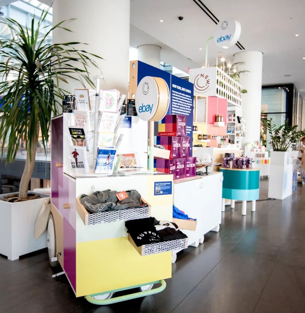 Colorful branded merchandise display cart featuring custom apparel, promotional products, and giveaway items for corporate events and trade shows in a modern retail space.