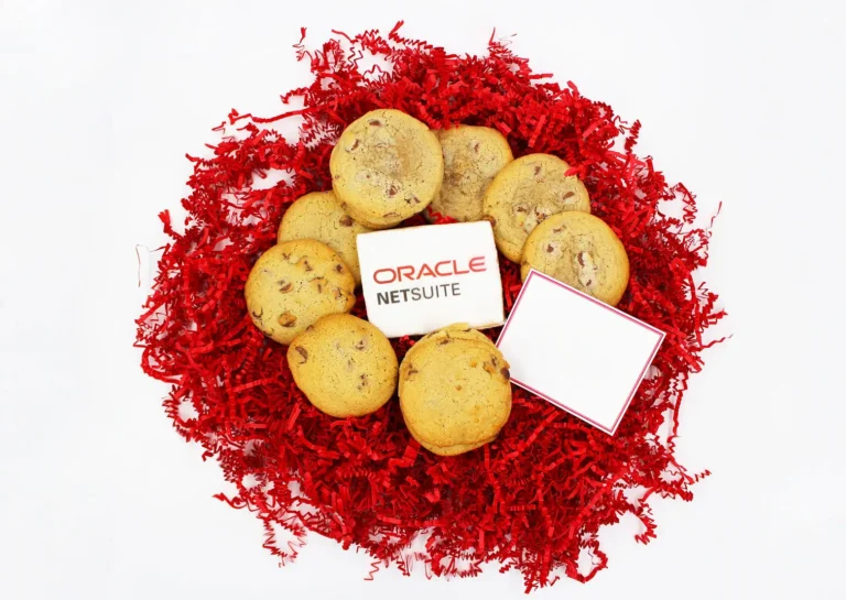 Custom branded chocolate chip cookies with Oracle NetSuite logo, surrounded by fresh cookies and red shredded paper, perfect for corporate gifts and event giveaways.